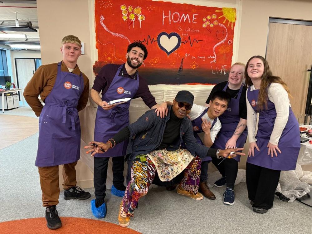 Volunteers in purple aprons laughing together in front of the Home mural